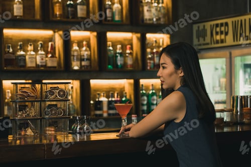 Preview: Asian woman drinking a cocktail at a bar at night.