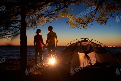 Preview: Couple man and woman having rest at tourist tent and burning campfire on sea shore near forest