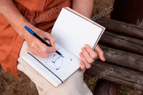 Preview: Close-up of female hands drawing express neurographic art in notebook outdoors