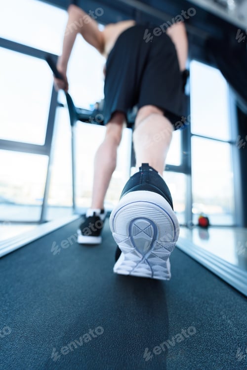 Preview: Close-up partial view of mature man in sportswear exercising on treadmill in gym