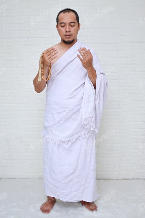 Preview: Full length shot of Asian muslim man wearing white ihram clothes and praying while holding prayer be