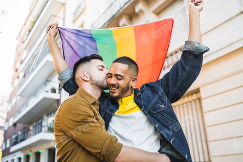 Preview: Gay couple embracing and showing their love with rainbow flag.