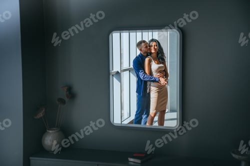 Preview: Passionate caucasian couple hugging reflected in mirror at home. bearded man embracing girlfriend