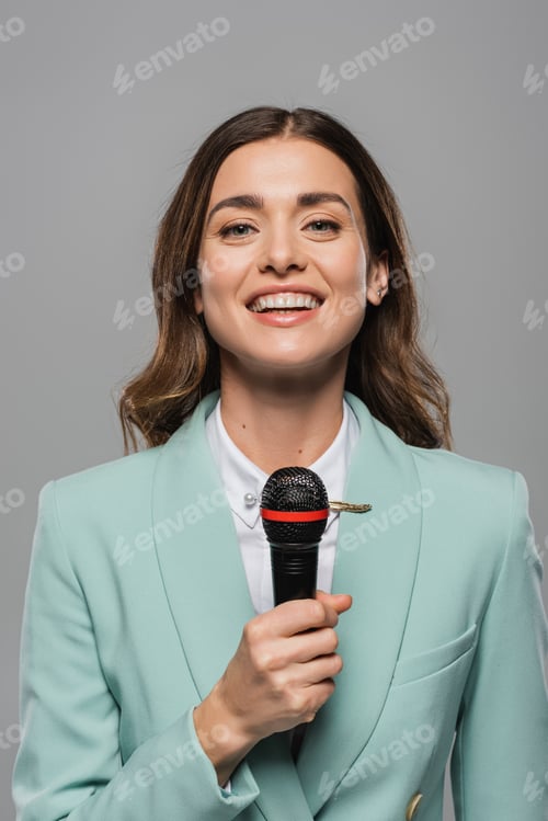 Preview: Portrait of smiling brunette event host in blue formal wear talking at wireless microphone