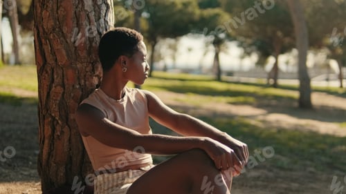 Preview: Lonely girl sitting under tall green trees in a park in the summertime
