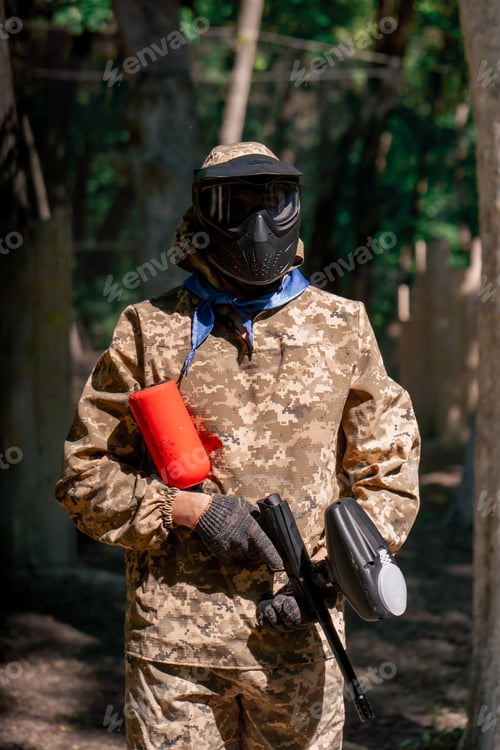 Preview: in the wild near tree structures player in a pintball uniform holds a pistol with a red balloon team
