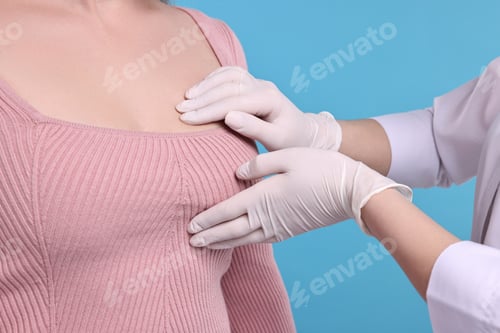 Preview: Mammologist checking woman's breast on light blue background, closeup