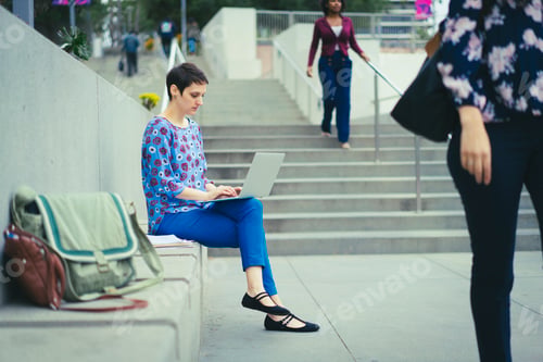 Preview: Young woman sitting outdoors, using laptop