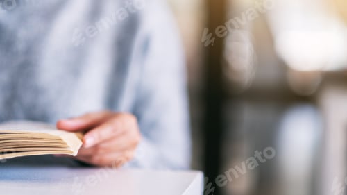 Preview: Closeup image of a woman holding and reading a vintage novel book on wooden table