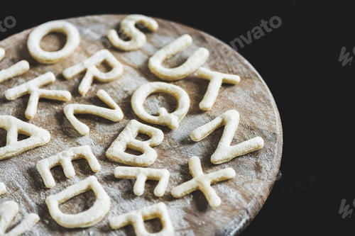 Preview: close up view of letters made from cookie dough on wooden board with flour isolated on black