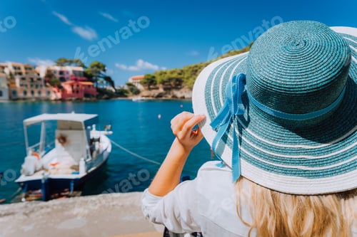 Preview: Happy young woman holding straw hat enjoying vacations in Assos village in front of emerald bay of
