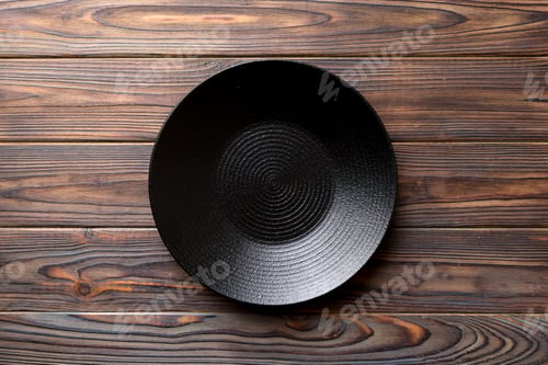 Preview: Top view of black plate on wooden background. Empty space for your design