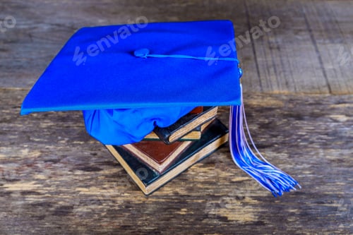 Preview: Graduation mortarboard on top of stack of books on abstract wood background