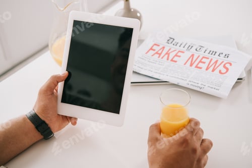 Preview: cropped view of man holding glass of orange juice and digital tablet with blank screen while sitting