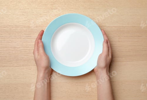 Preview: Woman with empty plate at wooden table, top view