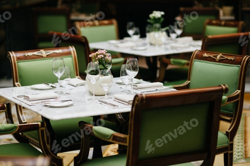 Preview: Table served with luxury glasses, cutlery, flowers, green chairs around in cozy restaurant