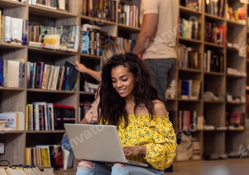 Preview: Portrait of young female student sitting at library using laptop with her friends in background.