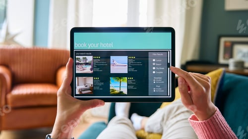 Preview: Close Up Of Woman Booking Holiday On Digital Tablet Lying On Sofa At Home