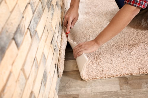 Preview: Man cutting new carpet flooring indoors, closeup. Space for text