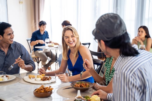 Preview: Group of diverse friend talking and eating food together in restaurant.