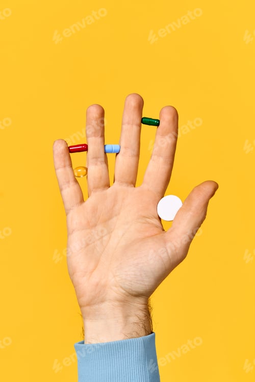 Preview: Male hand holding various pills balanced on fingers over yellow background