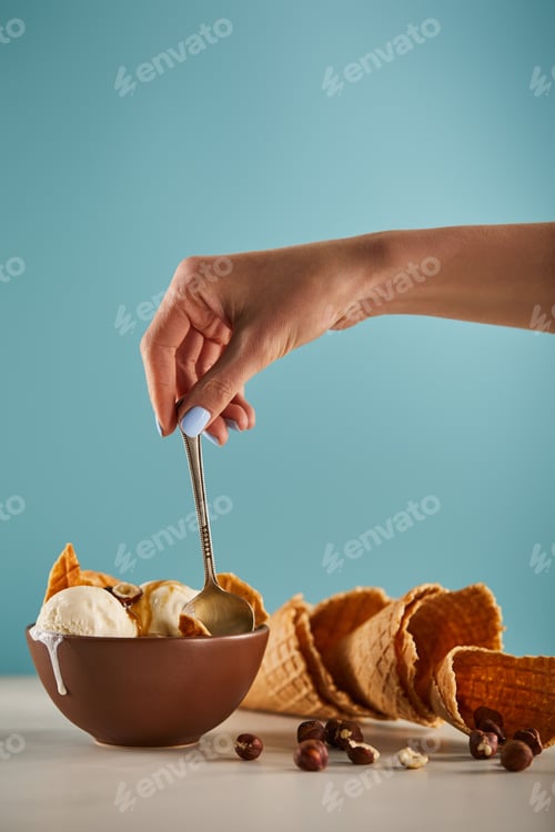 Preview: cropped view of woman with spoon, bowl of ice cream and waffle cones on blue