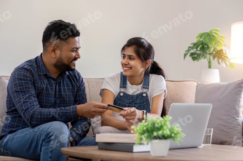 Preview: Happy couple using credit card to make online purchases on laptop in living room.