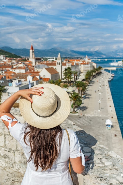 Preview: Rear view of woman standing on city walls looking at idyllic seaside town of Trogir, Croatia