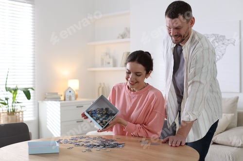 Preview: Happy couple solving puzzle together at wooden table indoors