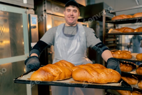 Preview: close up In a professional kitchen an inclusive baker stands with ready-made bread on a tray smiling