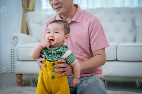 Preview: A man is holding a baby and smiling. The baby is wearing a yellow outfit. Scene is happy and joyful