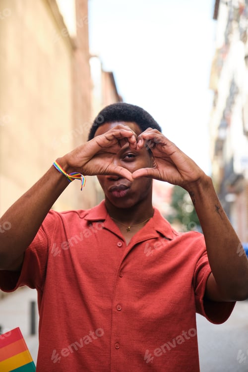 Preview: Gay black man in a red shirt holding his hands together in the shape of a heart.