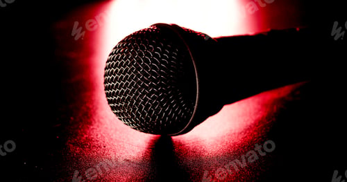 Preview: Close up of black microphone on a red light and black background.