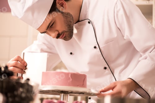Preview: focused confectioner making sweet cake in restaurant kitchen