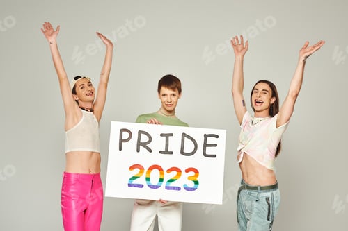 Preview: happy and tattooed gay men in colorful clothes standing with raised hands near queer friend holding