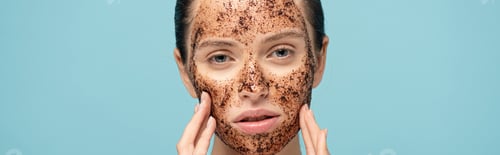 Preview: panoramic shot of attractive girl applying coffee scrub on face, isolated on blue