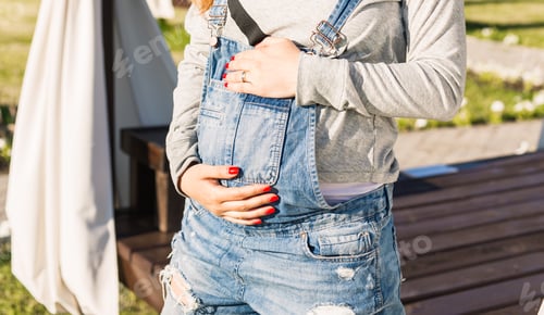 Preview: Young pregnant woman holds her hands on her swollen belly. Love concept.