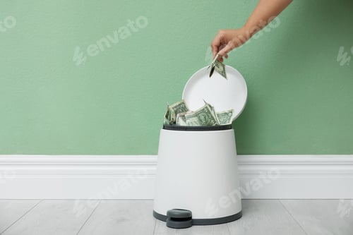 Preview: Woman throwing dollar banknotes into trash bin indoors, closeup. Space for text