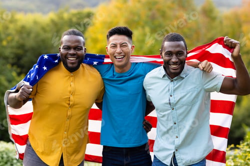 Preview: Portrait of happy diverse male friends covered with flag of usa in garden