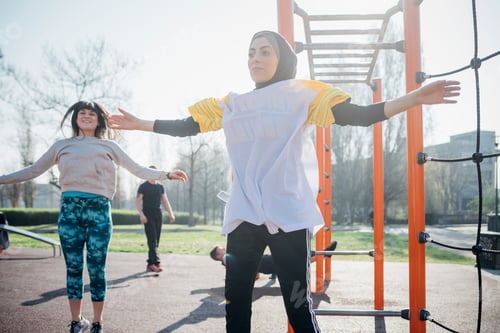 Preview: Calisthenics class at outdoor gym, young women jumping with arms outstretched