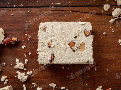 Preview: Halva slice with almonds on wooden table background, top view.