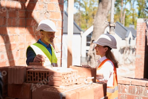 Preview: Male contractor talking to female architect near pile of bricks