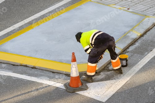 Preview: Worker painting a curb on a city road with a roller and yellow paint