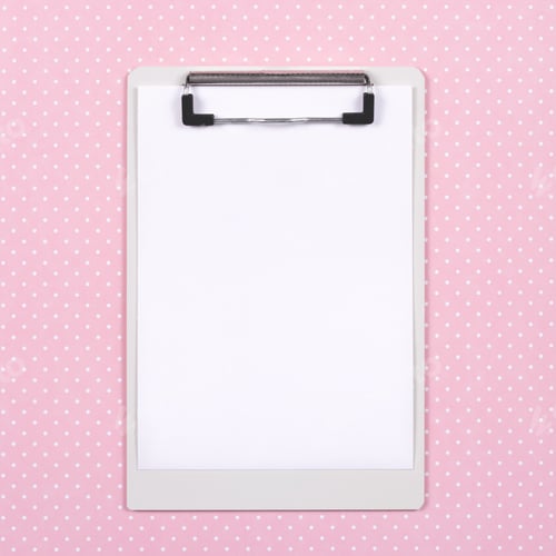 Preview: Top view of clipboard with white page on pink polka dot background.