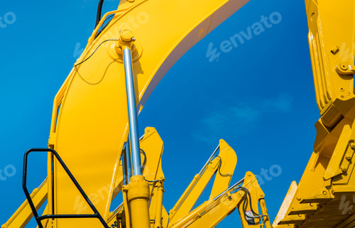 Preview: Yellow backhoe with hydraulic piston arm against clear blue sky. Heavy machine for excavation