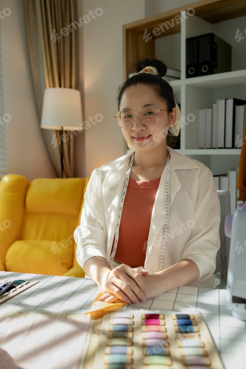 Preview: a charming designer is looking into the camera in her design studio, a lovely dressmaker is sitting