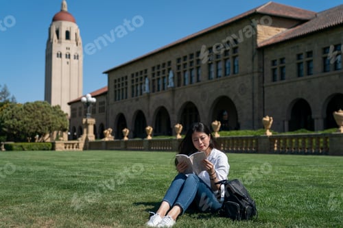 Preview: school girl reading on lawn near hoover tower