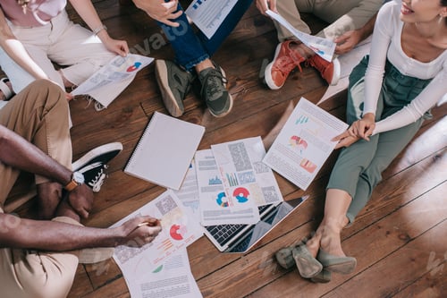 Preview: cropped view of young businesspeople sitting on floor near documents with infographics