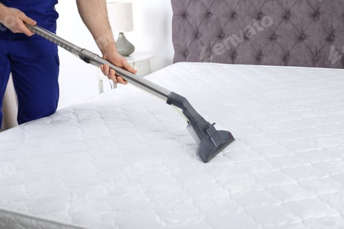 Preview: Man disinfecting mattress with vacuum cleaner, closeup