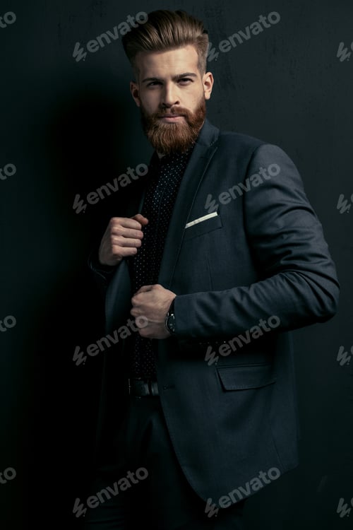 Preview: Stylish handsome bearded man in trendy suit posing on black